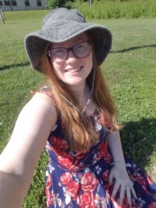 Katie sitting on grass in a hat